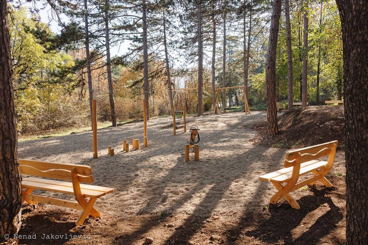Prirodno igralište među borovima: drvene klupe i greda za balansiranje